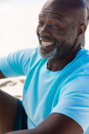 Cheerful african american bald senior man with white beard sitting at beach. unaltered, active...