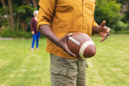 Midsection of african american senior man playing rugby with friends in backyard. unaltered, lifestyle, weekend, leisure, sport and active seniors.の写真素材