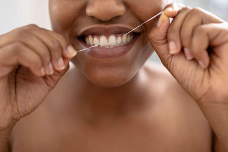 Close-up of african american mid adult woman using dental floss in bathroom. unaltered, dental health, lifestyle, hygiene, routine.の写真素材
