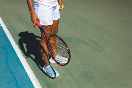 Low section of young female african american athlete standing with tennis racket and ball at court. unaltered, sport, competition and tennis game concept.の写真素材
