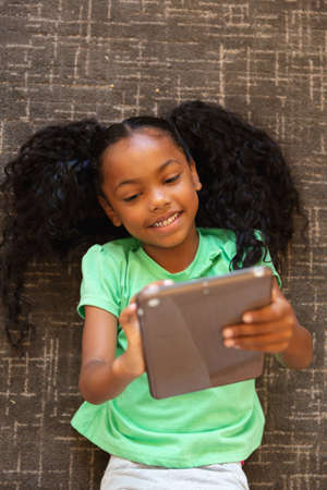 Overhead view of african american elementary girl using digital tablet while lying on carpet....