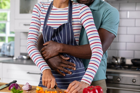 Midsection of african american young man embracing caucasian girlfriend cooking in kitchen at home. unaltered, lifestyle, leisure, love, togetherness, domestic life, food, preparing food.の写真素材