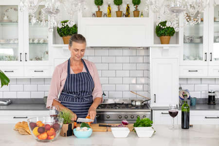 Senior caucasian woman cutting vegetables in kitchen at home. unaltered, lifestyle, retirement,...
