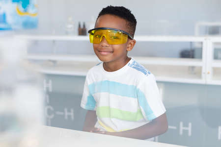 Portrait of african american elementary schoolboy wearing protective eyewear during chemistry class....