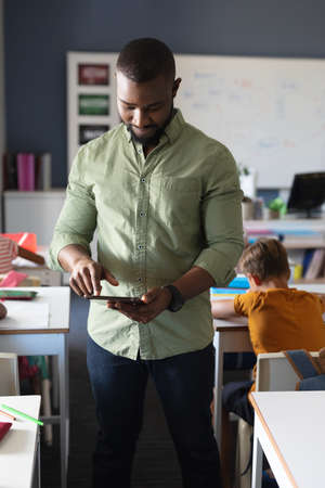 African american young male teacher using digital tablet while standing in classroom. unaltered, education, wireless technology, teaching, occupation and school concept.の写真素材