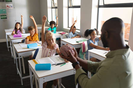 African american young male teacher showing brain model to multiracial students with hand raised....