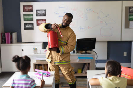 African american young male teacher in uniform showing fire extinguisher to multiracial students. unaltered, education, firefighter, safety, protection, teaching and school concept.の写真素材