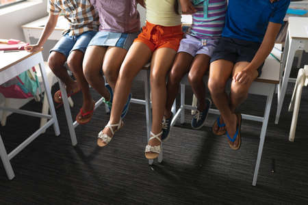 Low section of multiracial elementary school students sitting on desk in classroom. unaltered, education, childhood, learning, together and school concept.の写真素材