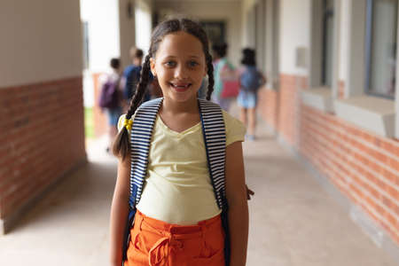 Portrait of happy caucasian elementary schoolgirl standing in corridor. unaltered, education, childhood and school concept.の写真素材