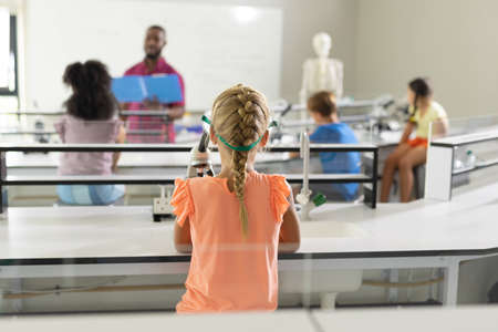 Rear view of multiracial elementary students listening to african american young male teacher in...