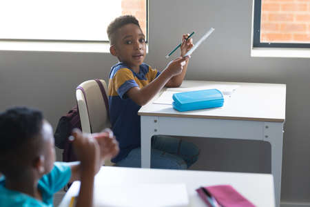 Portrait of african american elementary schoolboy with pencil and ruler sitting at desk in...