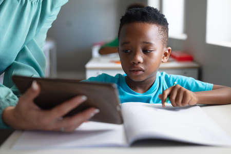 Close-up of caucasian young female teacher showing digital tablet to african american elementary boy. unaltered, education, childhood, occupation, technology, teaching and school concept.の写真素材