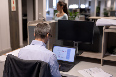 Rear view of mature caucasian businessman using laptop while working at modern workplace. unaltered,...