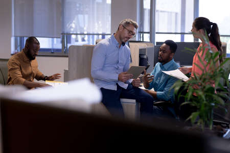 Caucasian businessman discussing over tablet pc with biracial colleagues at modern office....