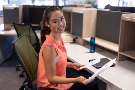 Portrait of smiling young female hispanic advisor sitting with documents at modern workplace....