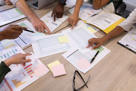 Cropped hands of multiracial advisors pointing at document in boardroom during meeting. unaltered,...
