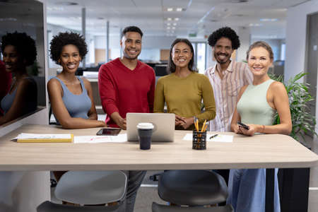 Team of happy male and female biracial advisors with laptop at desk during meeting in workplace. unaltered, business, teamwork, modern office and technology concept.の写真素材