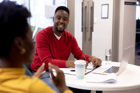 Smiling african american businessman discussing with businesswoman at modern workplace. unaltered,...