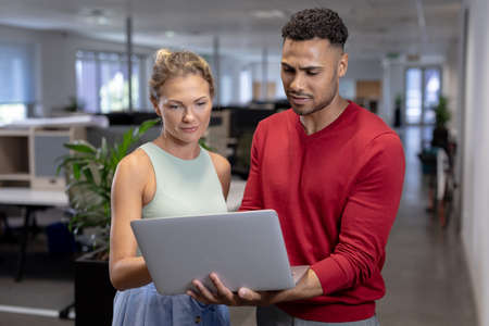 Multiracial business advisors discussing over laptop while standing at modern workplace. unaltered,...