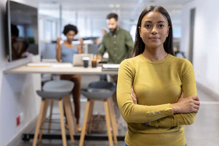 Portrait of confident young african american female advisor standing with arms crossed at workplace....