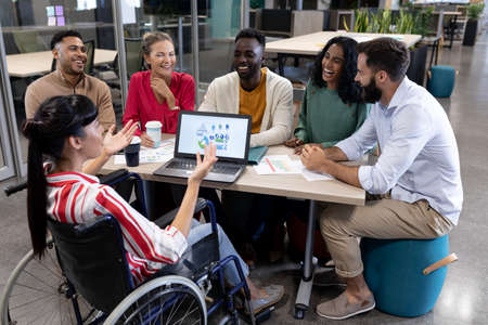 Disabled biracial businesswoman explaining strategy to happy colleagues during meeting. unaltered, physical disability, business, teamwork, modern office and technology concept.の写真素材