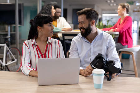 Happy multiracial business colleagues looking at each other while sitting with vr headset and...