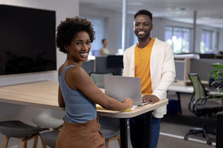 Portrait of smiling african american colleagues with laptop on desk working together in office....