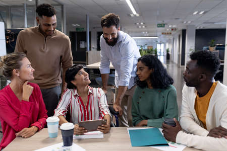Happy biracial male and female advisors discussing together during meeting in boardroom. unaltered, business, teamwork, modern office and technology concept.の写真素材