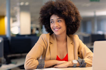 Happy young beautiful female african american advisor with afro hairstyle looking away at workplace....