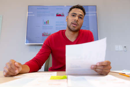 Portrait of confident male hispanic advisor with document explaining strategy in boardroom....