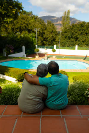 Rear view of biracial senior man with hand on wife's shoulder looking at view while sitting on steps. nature, unaltered, lifestyle, love, togetherness and retirement concept.の写真素材