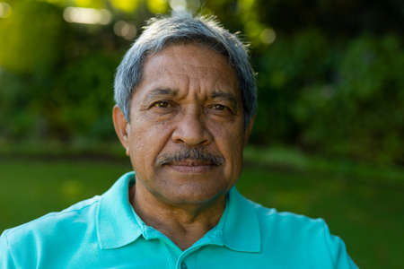 Close-up portrait of biracial serious senior man with gray hair against plants in park. nature,...