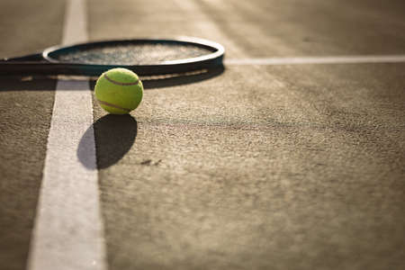 Surface level of tennis ball and racket on white lines at tennis court during sunset, copy space. sunlight, shadow, unaltered, sport, competition and racket sport concept.の写真素材
