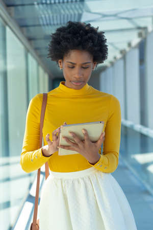 Confident beautiful african american female advisor using tablet pc in corridor at modern workplace....