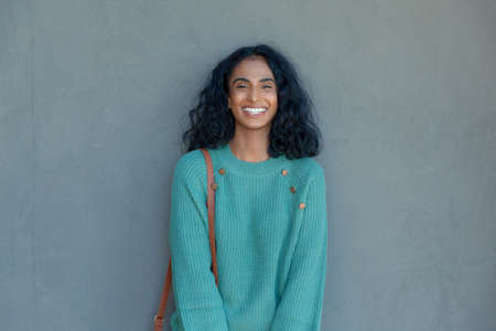 Portrait of happy young biracial businesswoman standing against gray wall with copy space....