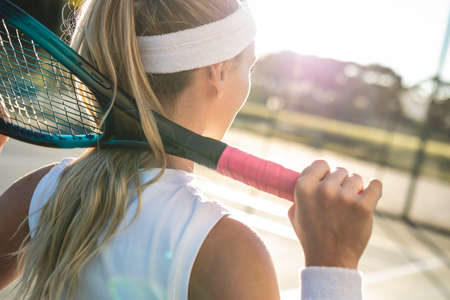Rear view of young blond caucasian female tennis player with racket around neck at court. unaltered,...