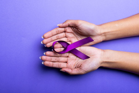 Cropped hands of african american mid adult woman with purple awareness ribbon over blue background. copy space, epilepsy, pancreatic cancer, medical, awareness, support, healthcare and alertness.の写真素材