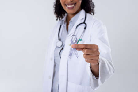 Midsection of happy african american mid adult female doctor with white lung cancer awareness ribbon. white background, lung, cancer, medical, ribbon, doctor, awareness, support, healthcare concept.の写真素材