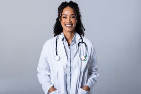 Portrait of happy african american mid adult woman with stethoscope and hands in pockets, copy space. white background, confidence, doctor, medical, healthcare, hospital and medical occupation.の写真素材