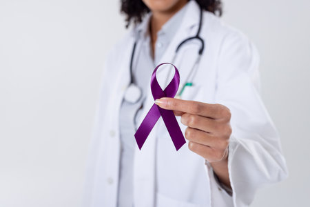 Midsection of african american mid adult female doctor holding purple cancer awareness ribbon. white background, epilepsy, pancreatic cancer, doctor, medical, awareness, support and healthcare.の写真素材