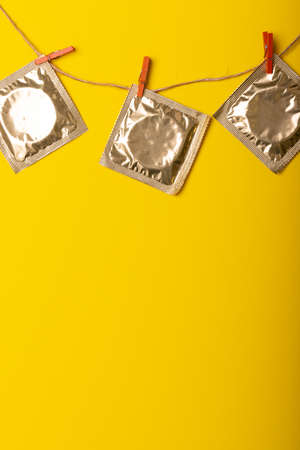 Close-up of condom packages hanging with clothespins on clothesline against yellow background. copy space, medical, std, aids, sexual, contraception, protection and healthcare concept,の写真素材