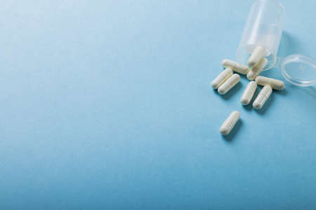 High angle view of white capsules spilled from bottle over blue background, copy space. capsule,...