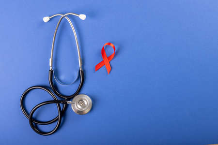 Directly above shot of stethoscope with red aids awareness ribbon over blue background, copy space. hiv, aids, red, medical, disease, ribbon, awareness, support, healthcare and alertness concept.の写真素材