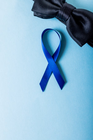 Directly above shot of blue prostate cancer awareness ribbon with black bowtie on blue background....
