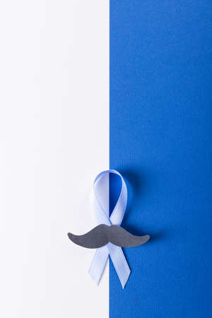 Overhead view of paper mustache and blue prostate cancer awareness ribbon on white, blue background. copy space, prostate, cancer, mustache, medical, awareness, support, healthcare and alertness.の写真素材