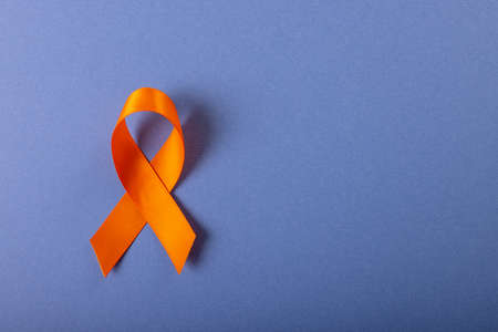 Directly above shot of orange leukemia awareness ribbon isolated against blue background, copy space. medical, leukemia, cancer, blood cell, awareness, support, healthcare and alertness concept.の写真素材