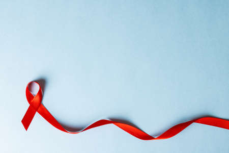 Directly above shot of red aids awareness ribbon isolated against blue background, copy space. hiv, aids, red, medical, disease, ribbon, awareness, support, healthcare and alertness concept.の写真素材