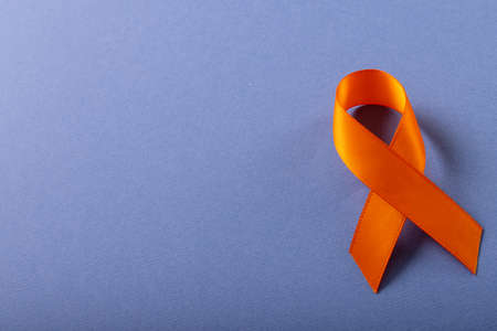 Overhead view of orange leukemia awareness ribbon isolated against blue background, copy space....