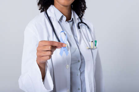 Midsection of african american mid adult female doctor holding blue stomach cancer awareness ribbon....