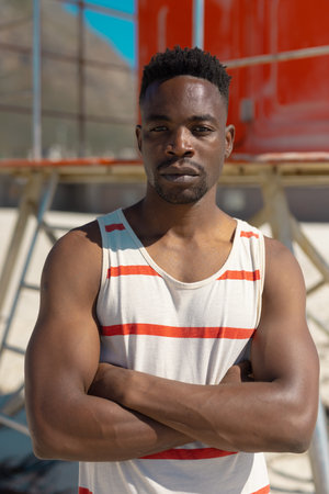 Portrait of handsome confident african american young man with arms crossed standing at beach. summer, unaltered, beach, lifestyle, enjoyment and holiday concept.の写真素材